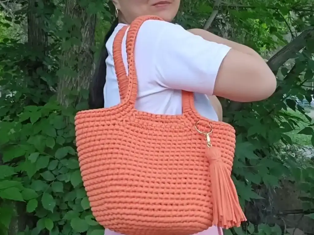 A woman models a trendy crochet trapezoid bag. The bag is slung comfortably over her shoulder, showcasing its versatile and practical design.