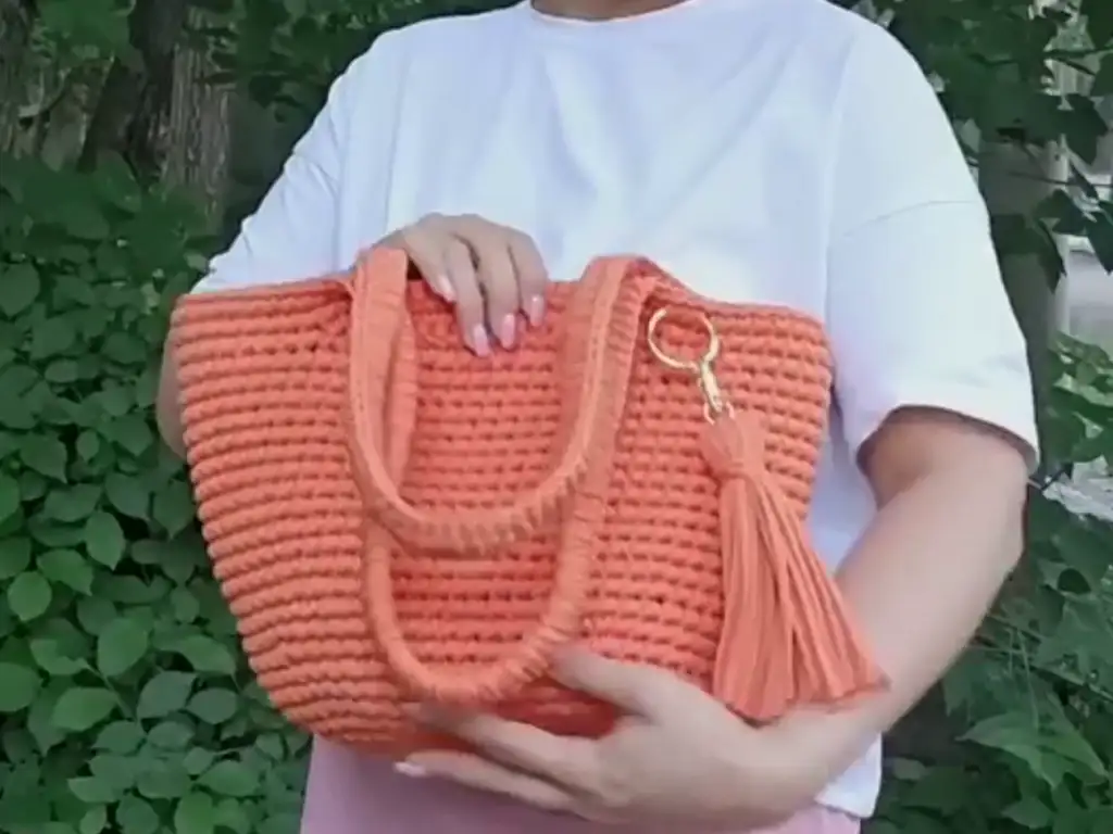 Close-up of a stylish, handmade trapezoid crochet bag. The bag is a vibrant orange color and features a spacious interior, perfect for everyday use