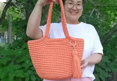 Close-up of a stylish, handmade trapezoid crochet bag. The bag is a vibrant orange color and features a spacious interior, perfect for everyday use.