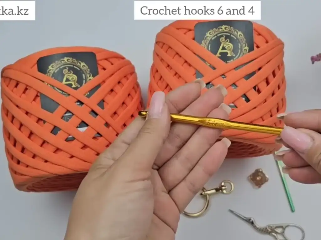 Materials needed for trapezoid crochet bag: orange yarn, crochet hooks, magnetic button, tassel ring