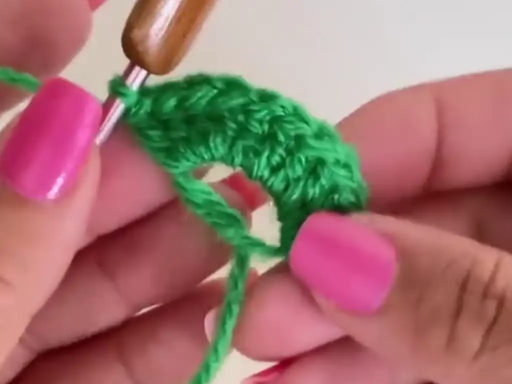 A hand crocheting a green circular base using single crochet stitches, forming the foundation for the rose stem.