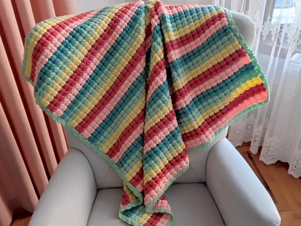 The finished crochet baby blanket draped over an armchair, showcasing its size and drape.