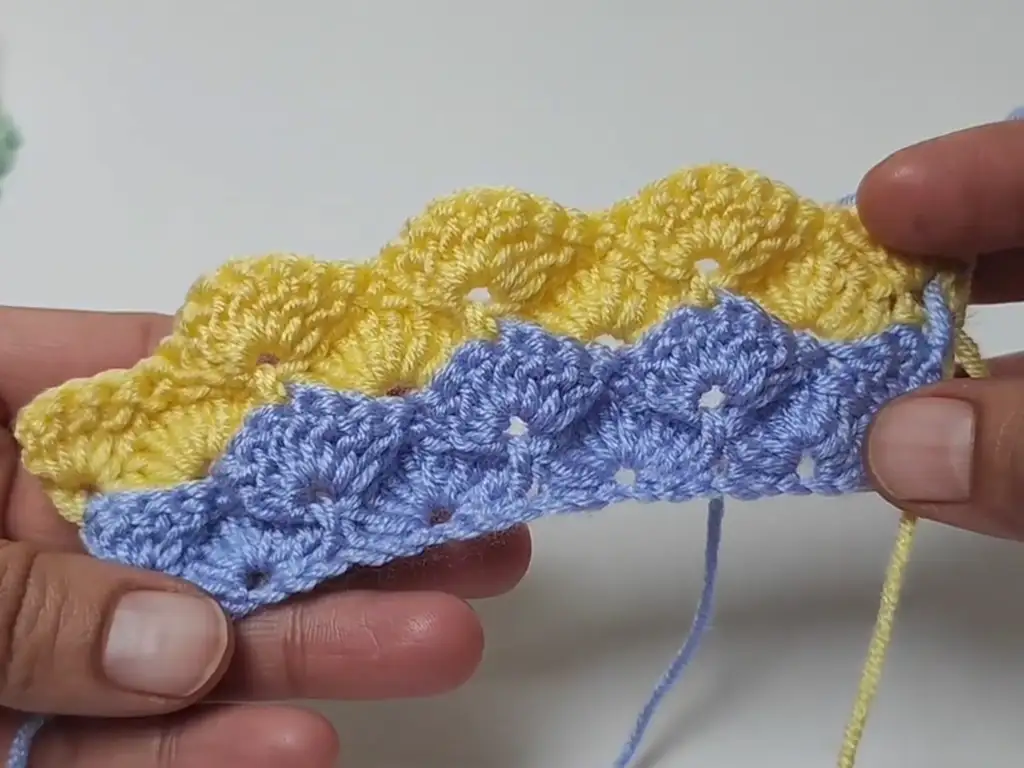 A partially completed crochet baby blanket, demonstrating a color change from pastel purple to pastel yellow yarn.