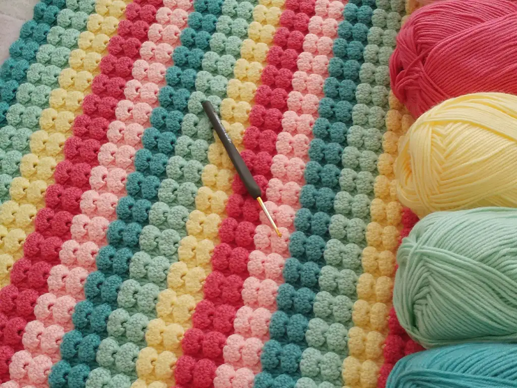 A close-up of the completed crochet baby blanket with the hook and yarn skeins used to create it.