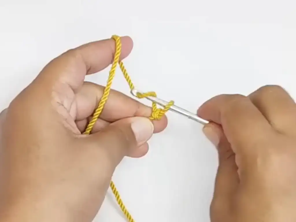 Hands holding a crochet hook and yarn, making a starting knot.