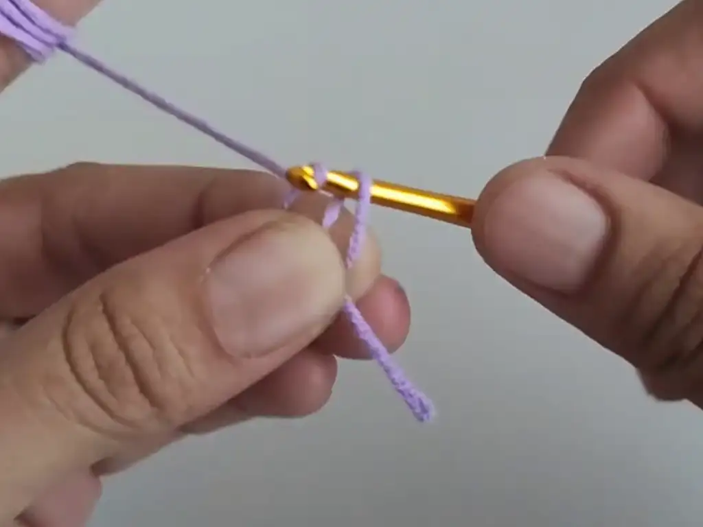 Creating the starting chain with a crochet hook and purple yarn for the Baktus shawl pattern.