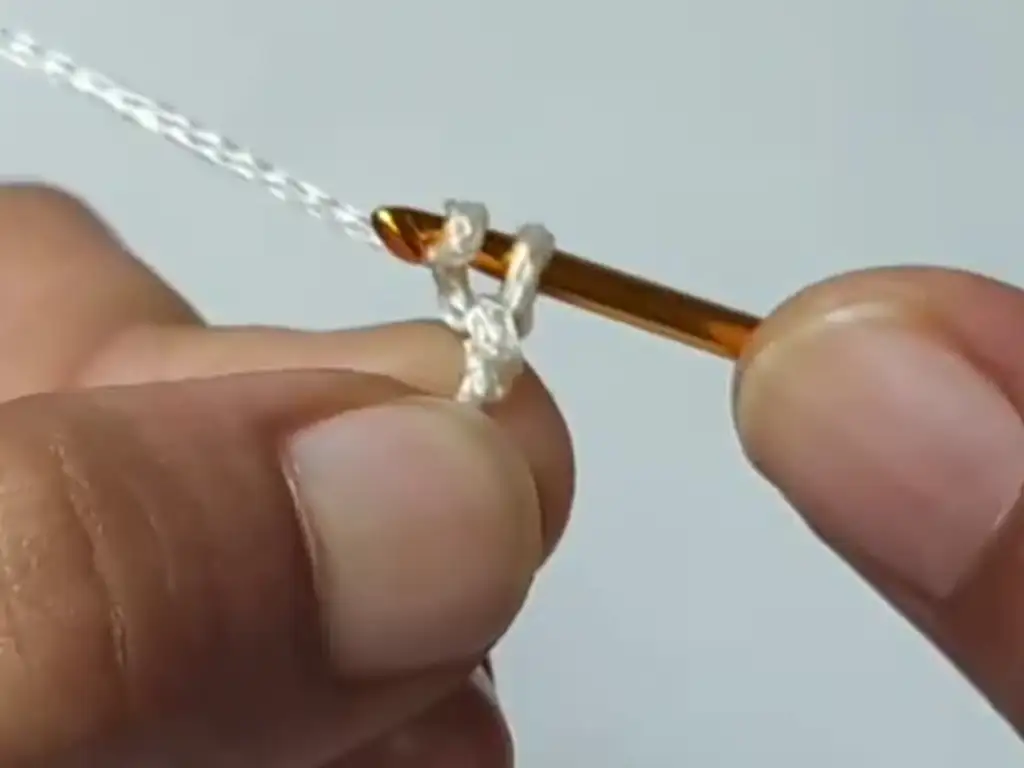 Close-up of hands making a chain stitch with a crochet hook and cream macrame yarn.