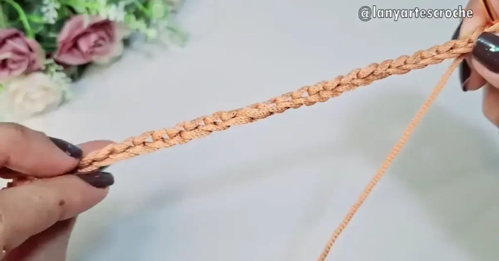 Close-up of a crocheter's hands creating a chain stitch with peach-colored yarn.