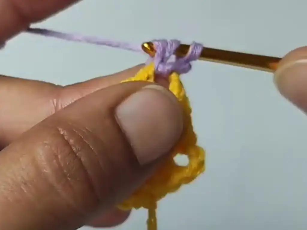 Demonstrating how to change colors in a crochet granny square, using purple yarn.