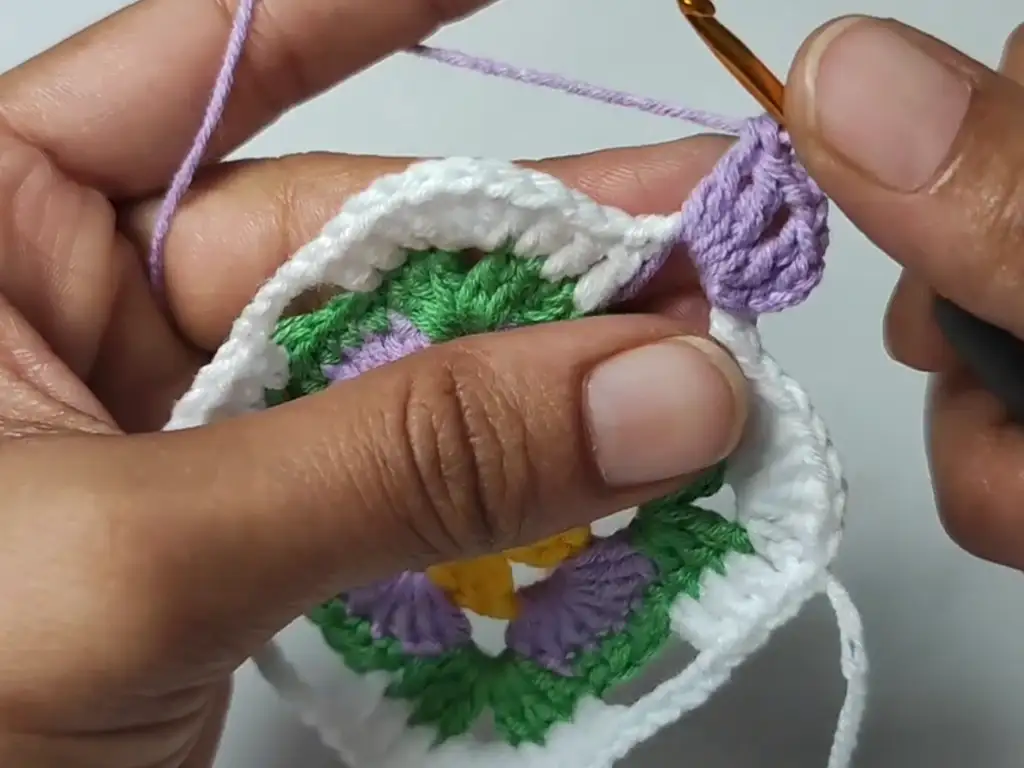 Crocheting the fifth round of a granny square, using purple yarn to create a repeating color pattern.