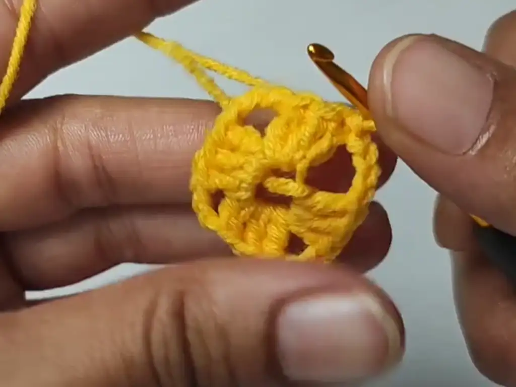 The first round of a crochet granny square, worked with yellow yarn.
