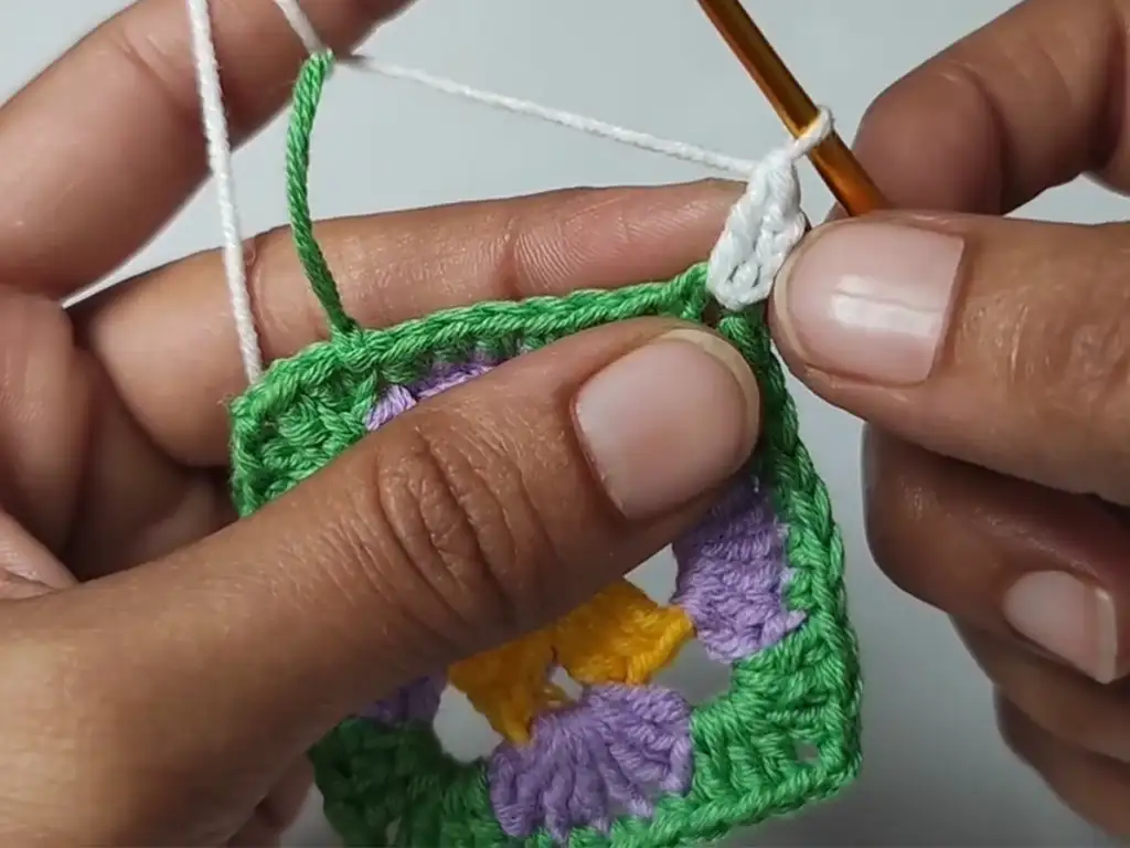 Starting the fourth round of a crochet granny square using white yarn.