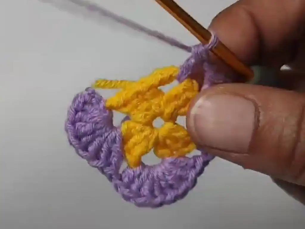 The second round of a crochet granny square completed, showcasing a color change to purple.