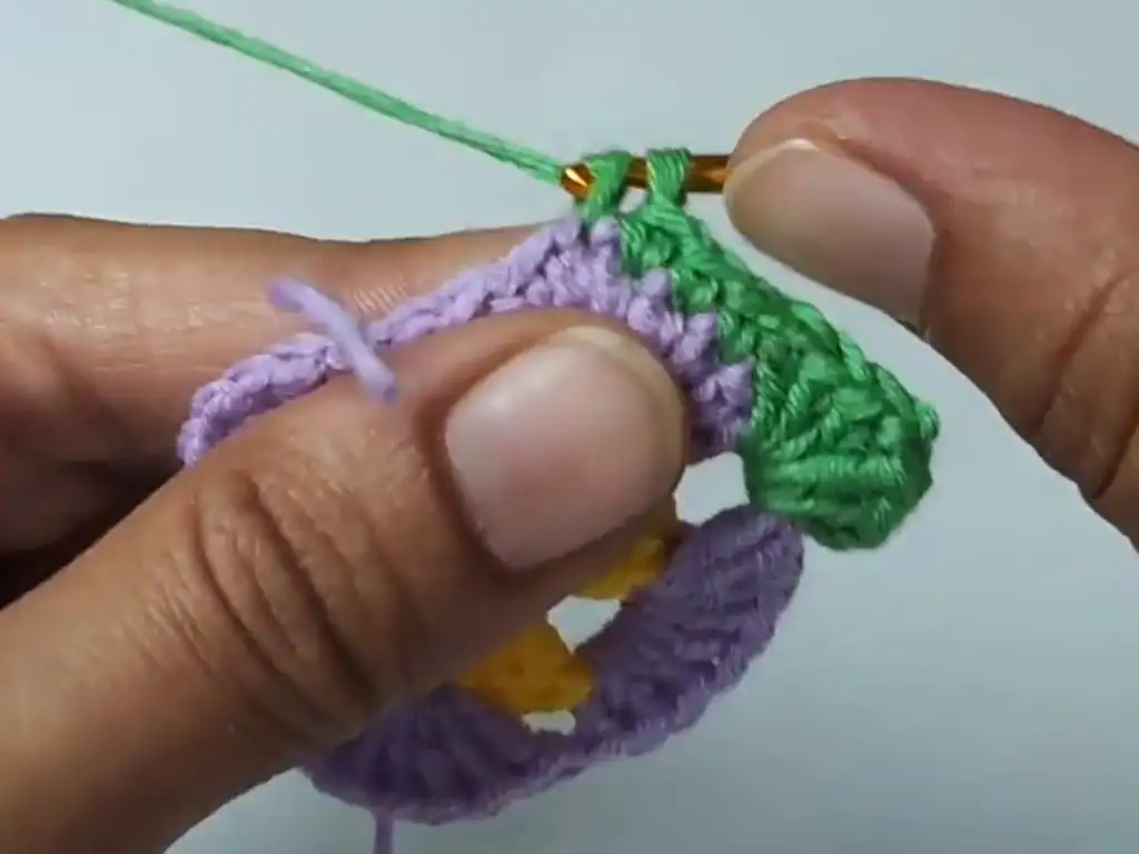 Working the third round of a crochet granny square, introducing green yarn for a vibrant color scheme.