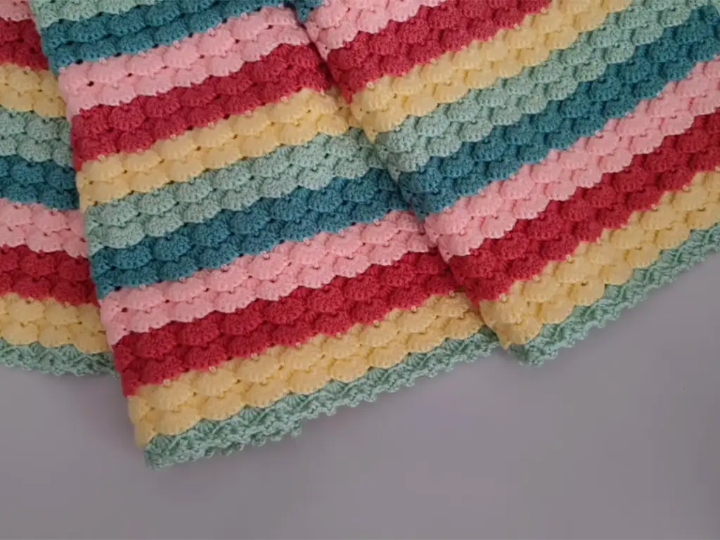 A completed crochet rainbow baby blanket folded neatly, showcasing stripes of pastel pink, green, yellow, and blue.