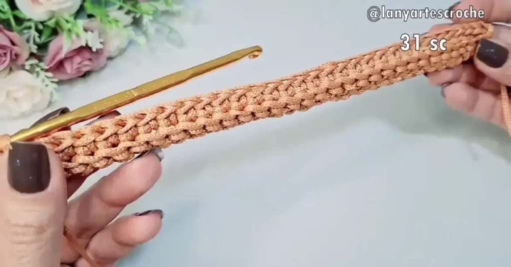 A row of single crochet stitches worked with a gold crochet hook and peach yarn.