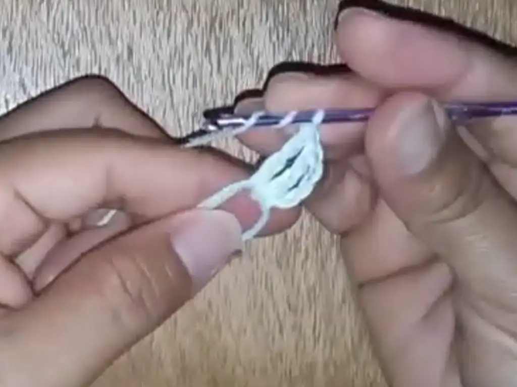 Close-up of a crocheter's hands using a slip stitch to join two white crochet squares, a crucial step in creating a crochet dress.
