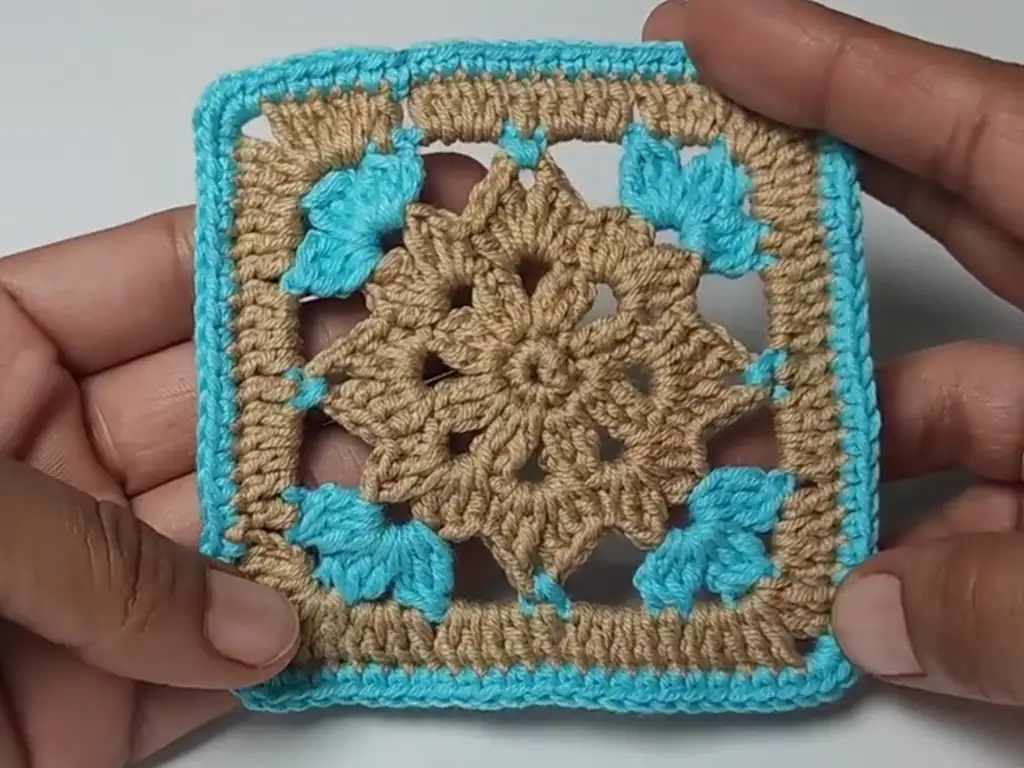 Finished crochet square motif with a beige center and blue border.