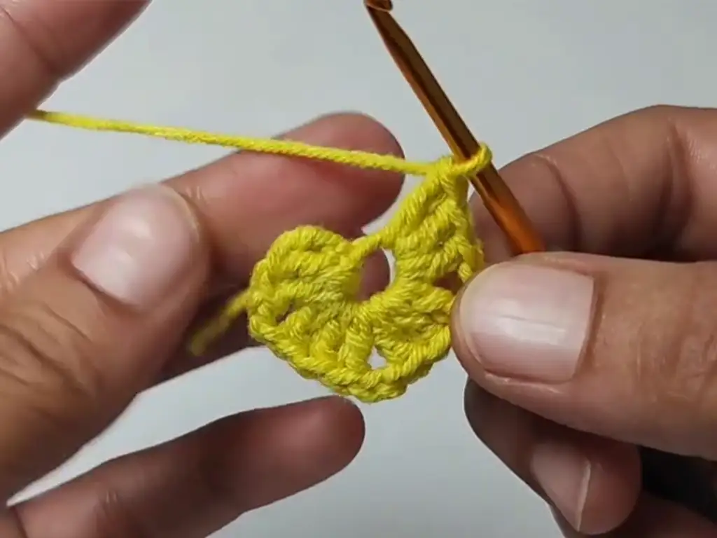 Working the first round of a granny square pattern with yellow yarn, showing the beginning chain stitches and double crochet clusters.