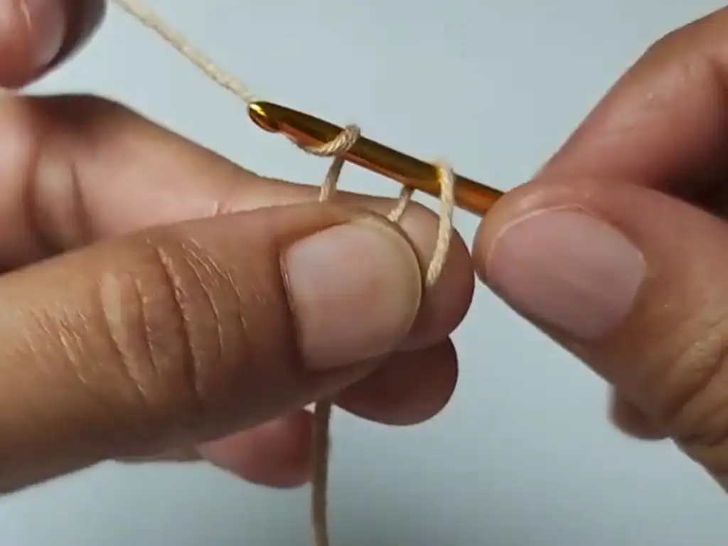 Creating a magic ring with beige yarn and a crochet hook.