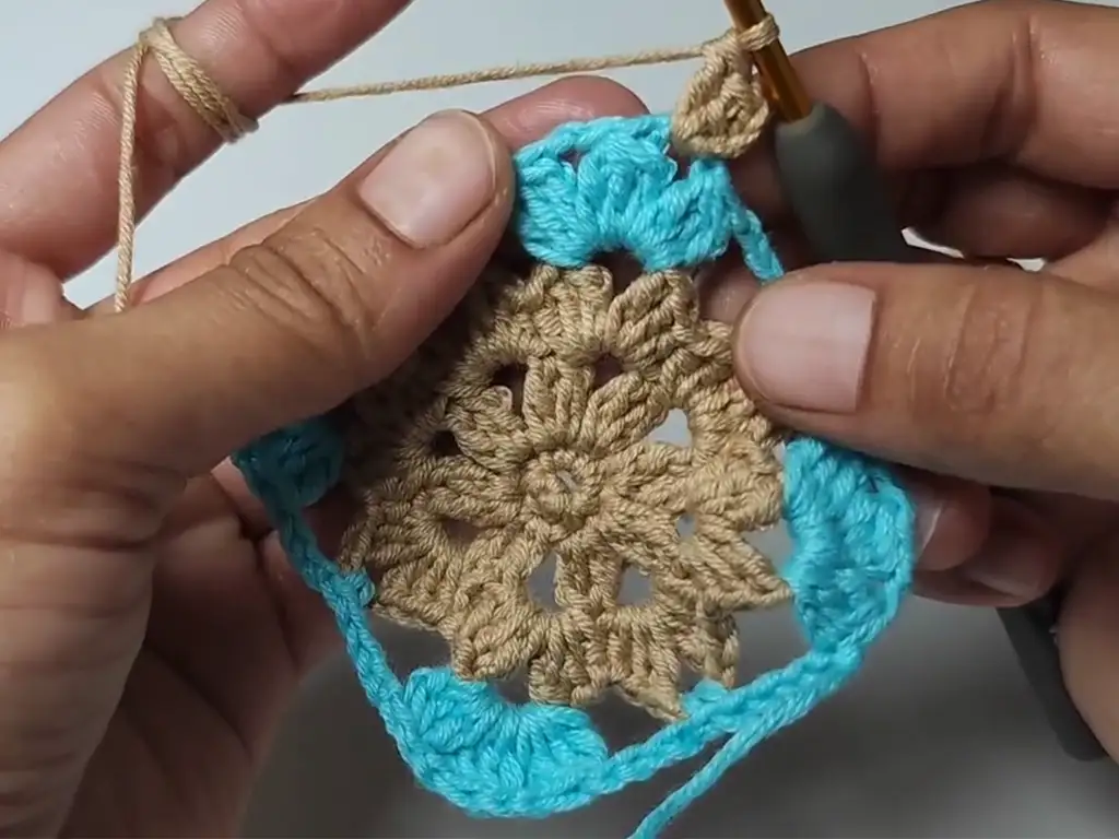 Completed third round of the crochet square pattern with blue corners.