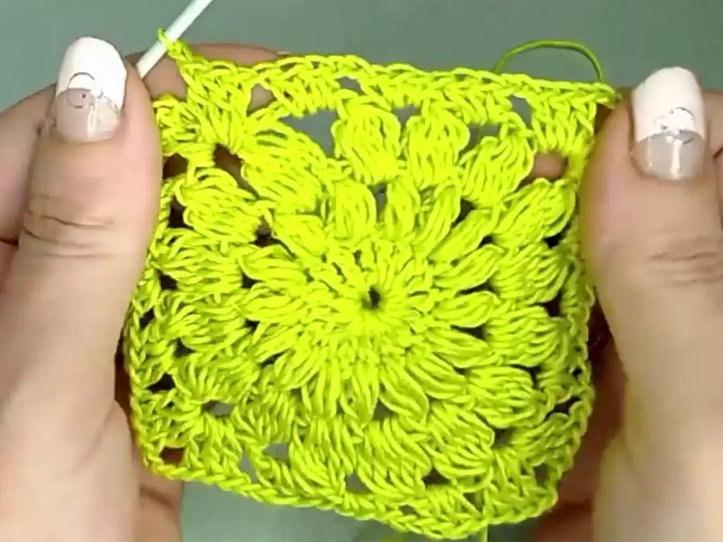 Completed bright green granny square with a delicate floral pattern, held in hands.