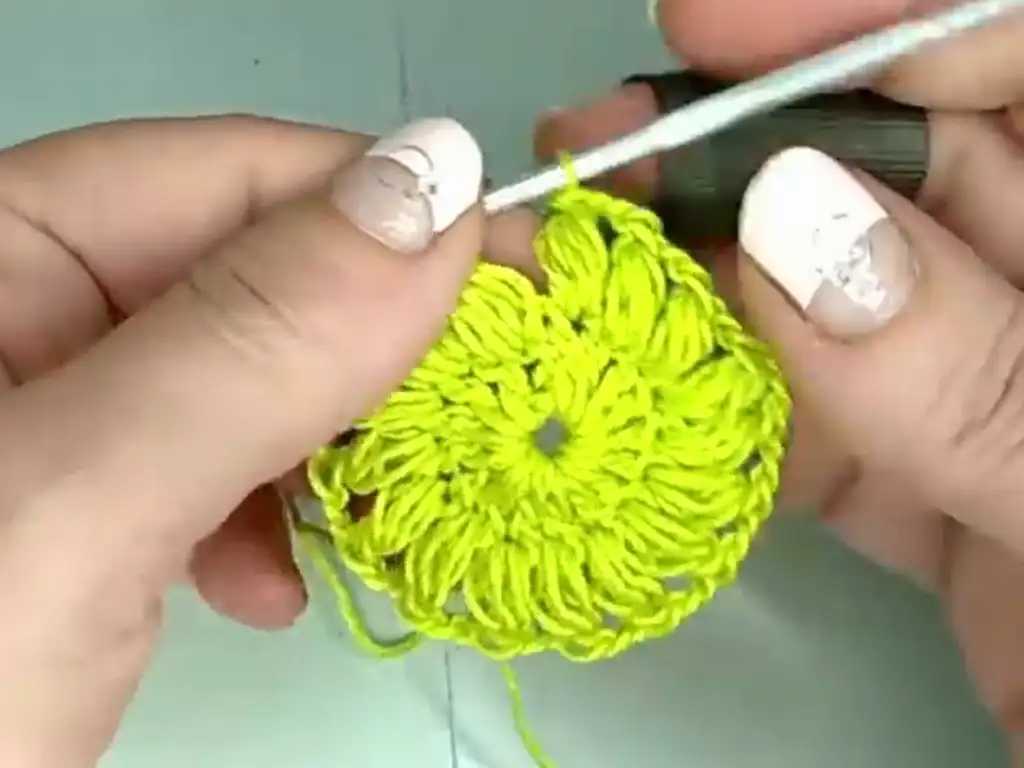 Hands crocheting the center of a bright green granny square with a floral pattern.