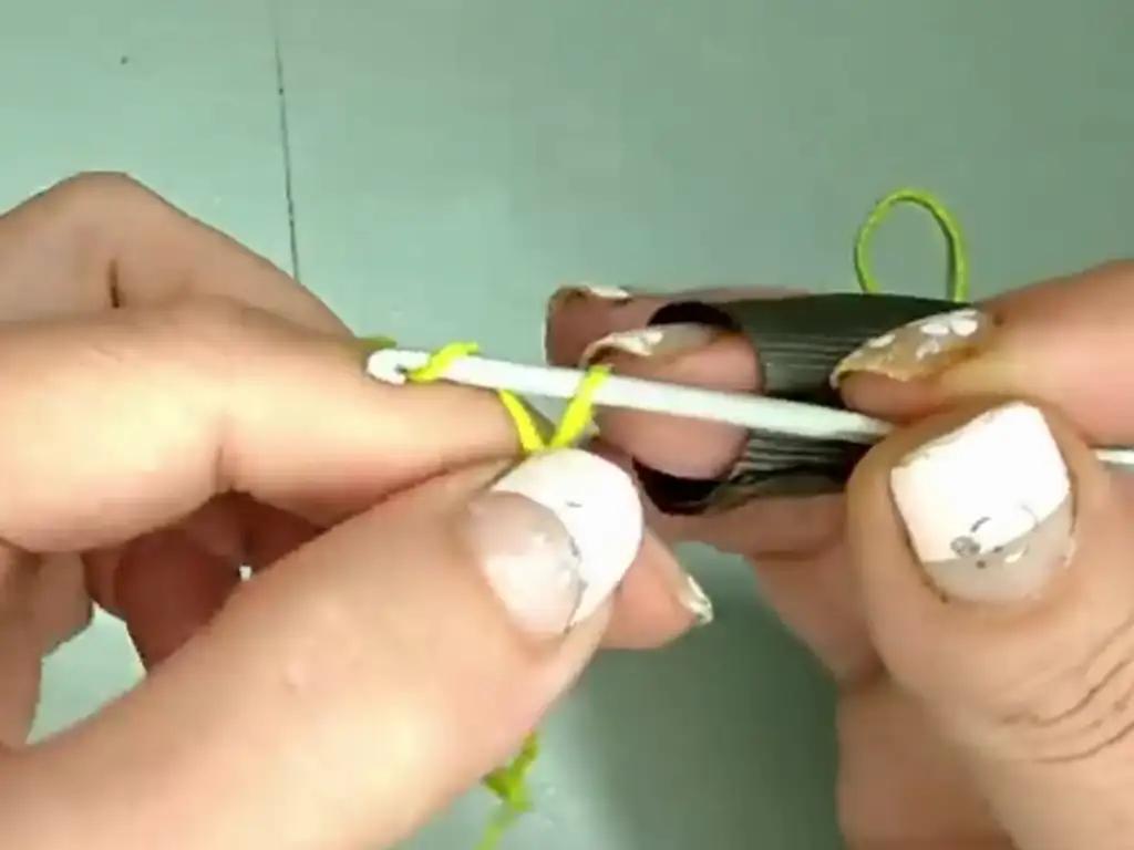 Close-up of hands holding a crochet hook and green yarn, beginning a chain stitch.
