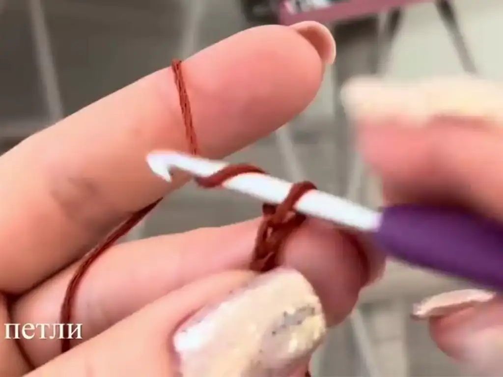 Close-up of a crochet hook with a starting chain in brown yarn, beginning a crochet tunic project.