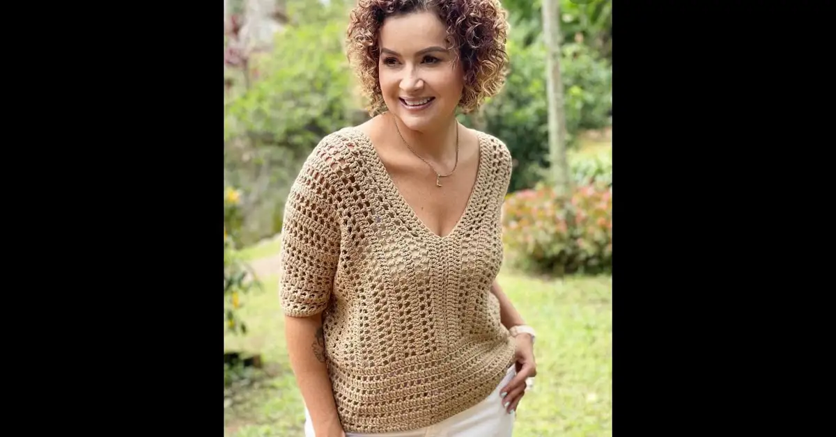 A woman models a stylish, beige crochet blouse with a v-neck and short sleeves, showcasing the beautiful drape and stitch definition of the easy crochet pattern.