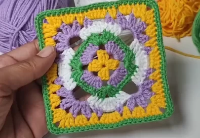 A completed crochet granny square held in hand, demonstrating its vibrant colors and perfect square shape.