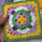 A completed crochet granny square held in hand, demonstrating its vibrant colors and perfect square shape.
