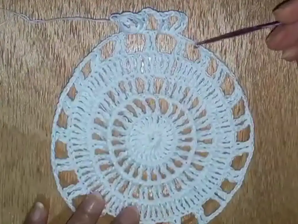A completed white crochet square motif, featuring a lacy openwork design, ready to be joined with other squares to form a dress.