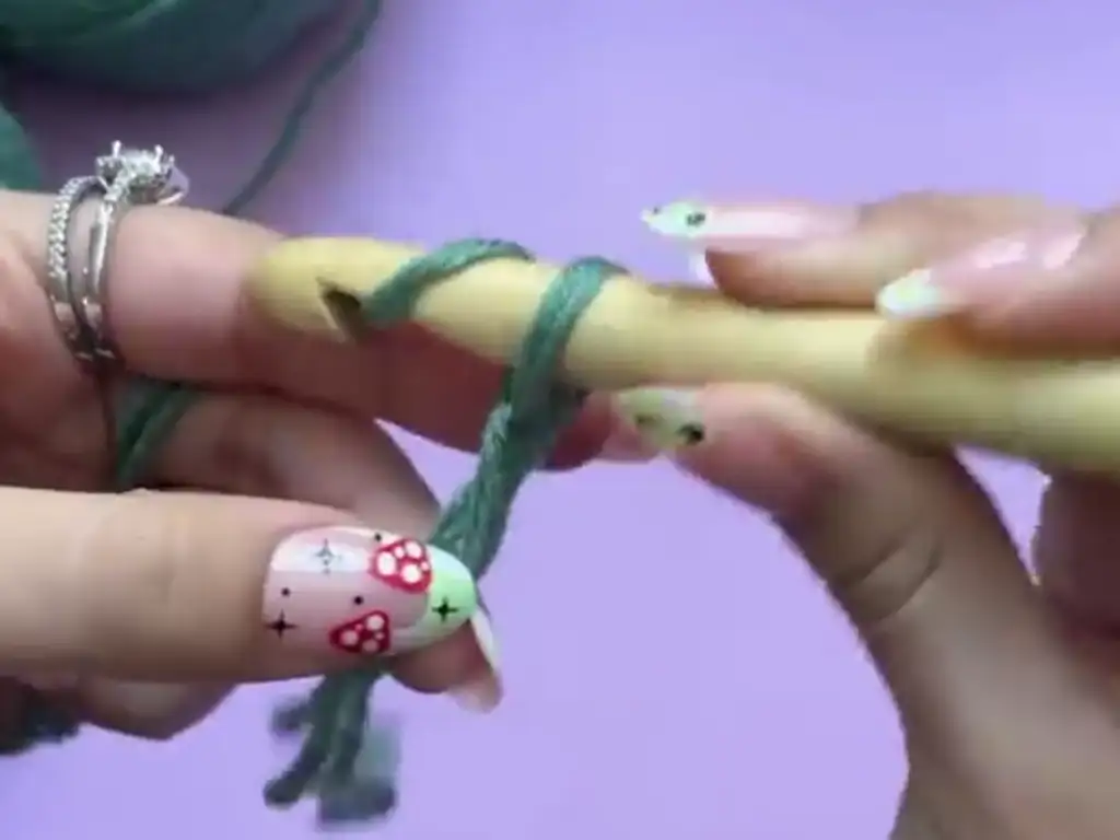 Close-up of hands making a slip knot with green yarn and a crochet hook.