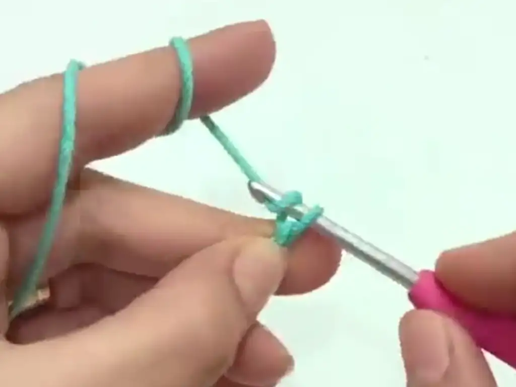 Demonstrating the initial step of the crochet phone case pattern, creating a magic ring with turquoise yarn.