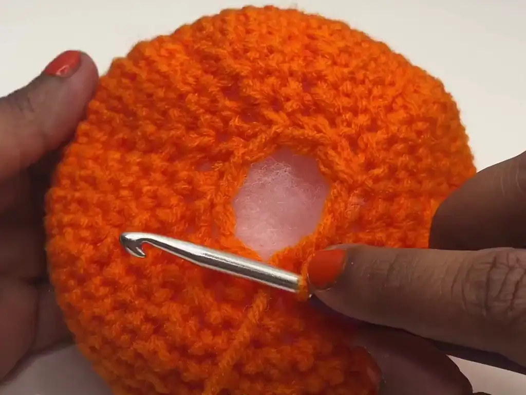 Stuffing the crochet pumpkin with polyfill to give it a plump shape.
