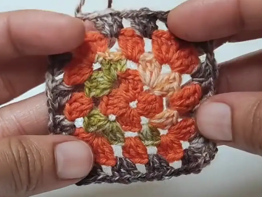 A completed crochet square motif with orange, green, and brown stripes.