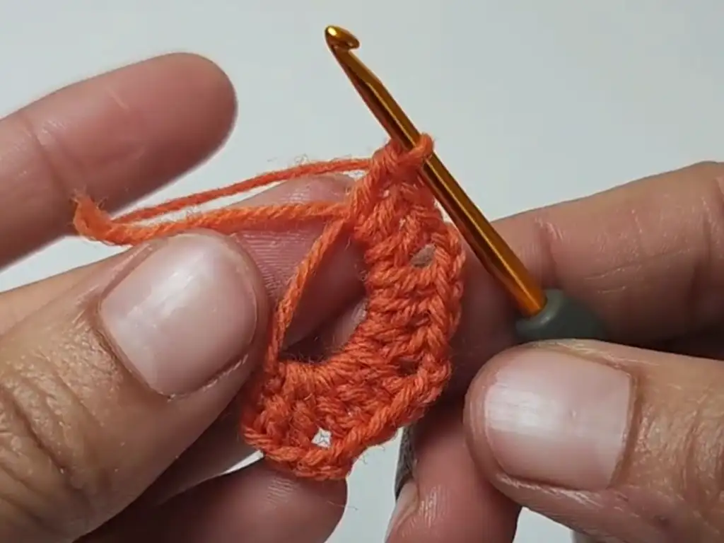 Hands crocheting the first round of a square motif with orange yarn.