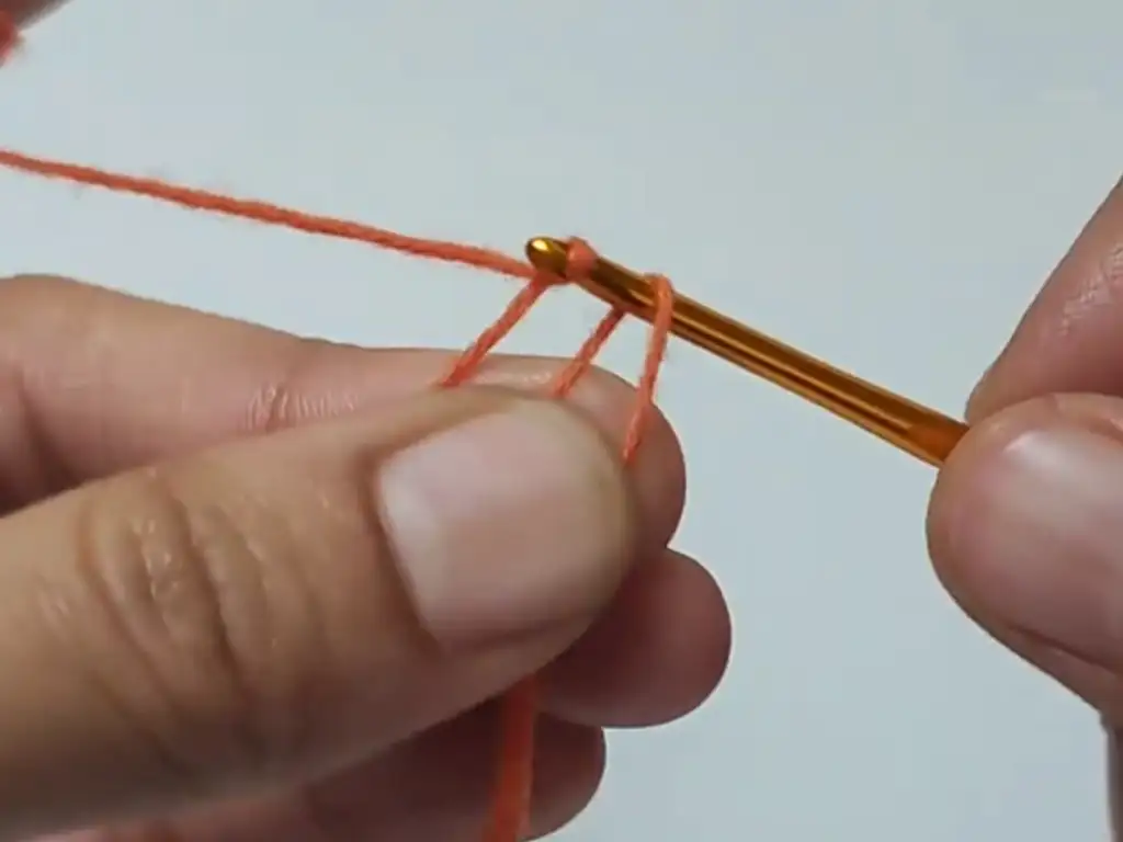 Close-up of hands crocheting a magic ring with orange yarn.