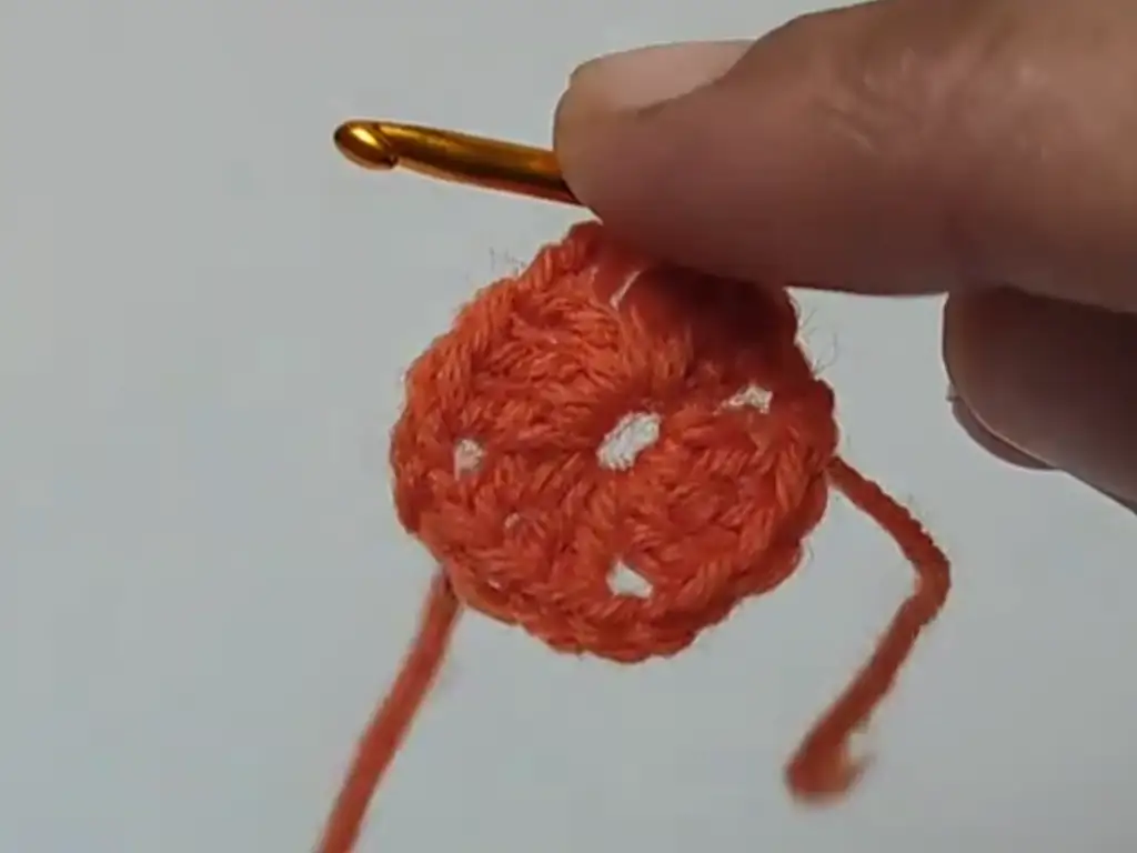 A completed first round of a crochet square motif in orange yarn.