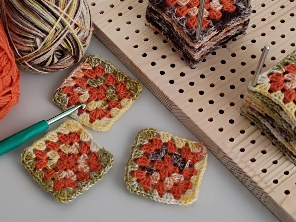 Multiple colorful crochet square motifs being blocked on a blocking board.