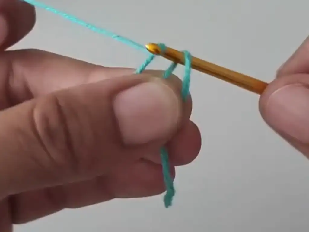 Creating a magic ring with turquoise yarn using a crochet hook. The foundation of the Geometric Crochet Square.