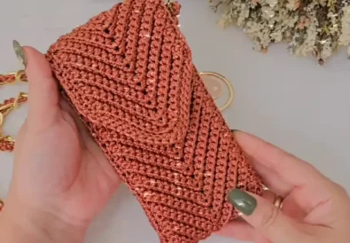 Finished crochet phone case in a stylish rust color with a gold chain strap.