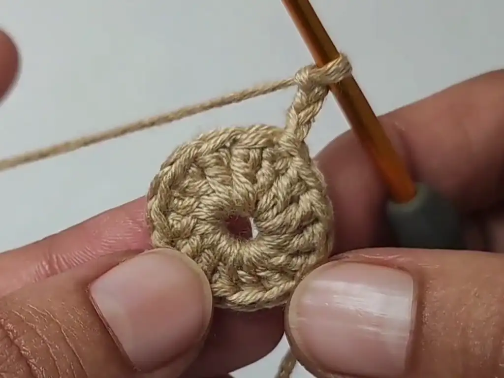 The first round of a crochet coaster completed, forming a small circle.