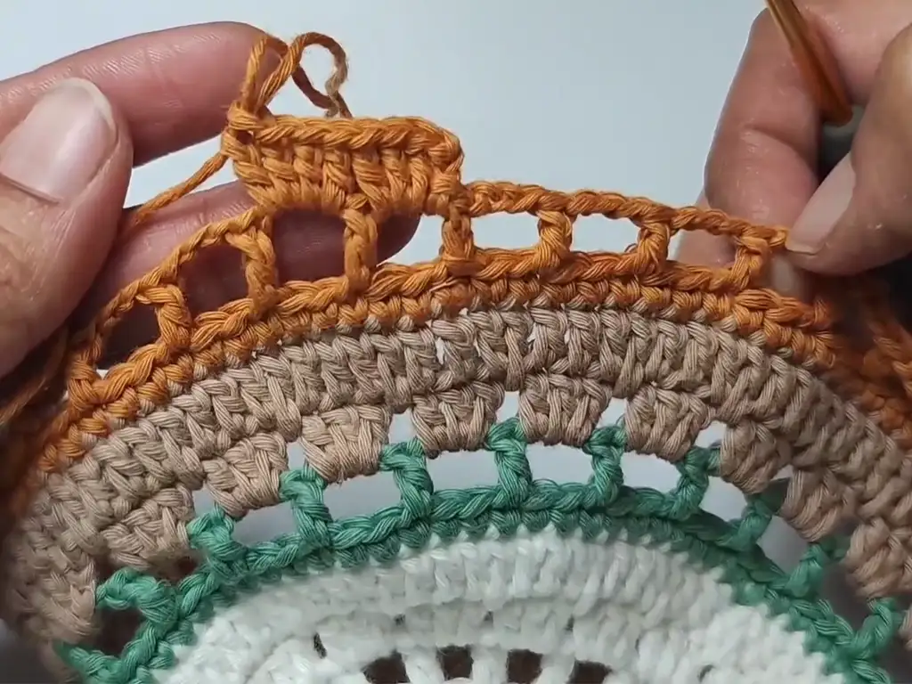 Crocheting a round of the placemat with orange yarn, creating chain spaces.