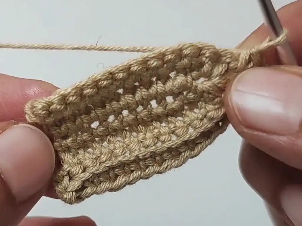 A hand crocheting the foundation chain, a crucial step in determining the length of the crochet pumpkin leaf.