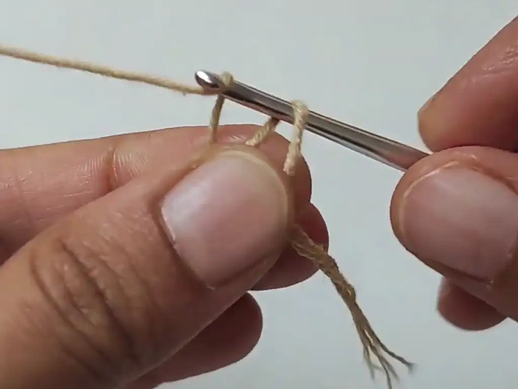 A close-up view of a hand making a slip knot, the first step in the crochet pumpkin leaves pattern.