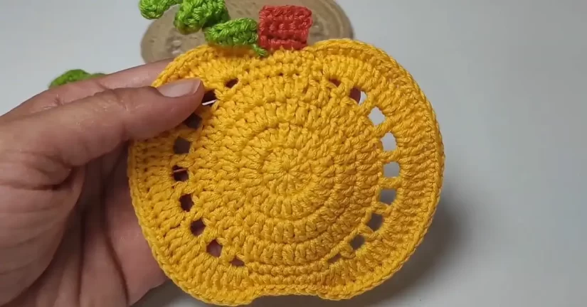 Close-up of a handmade yellow crochet pumpkin coaster, showcasing the stitch detail and pumpkin segments.