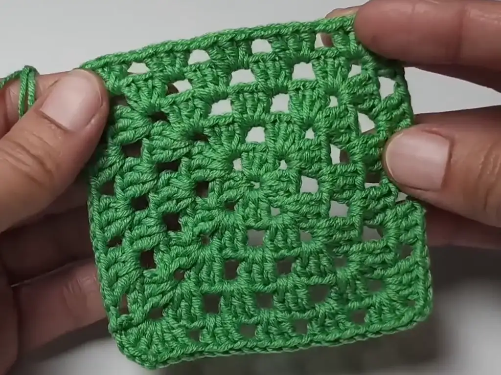 A completed crochet granny square, ready to be shaped into a Christmas tree ornament.