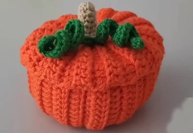 A finished orange crochet pumpkin basket with a lid, stem, and green leaves.